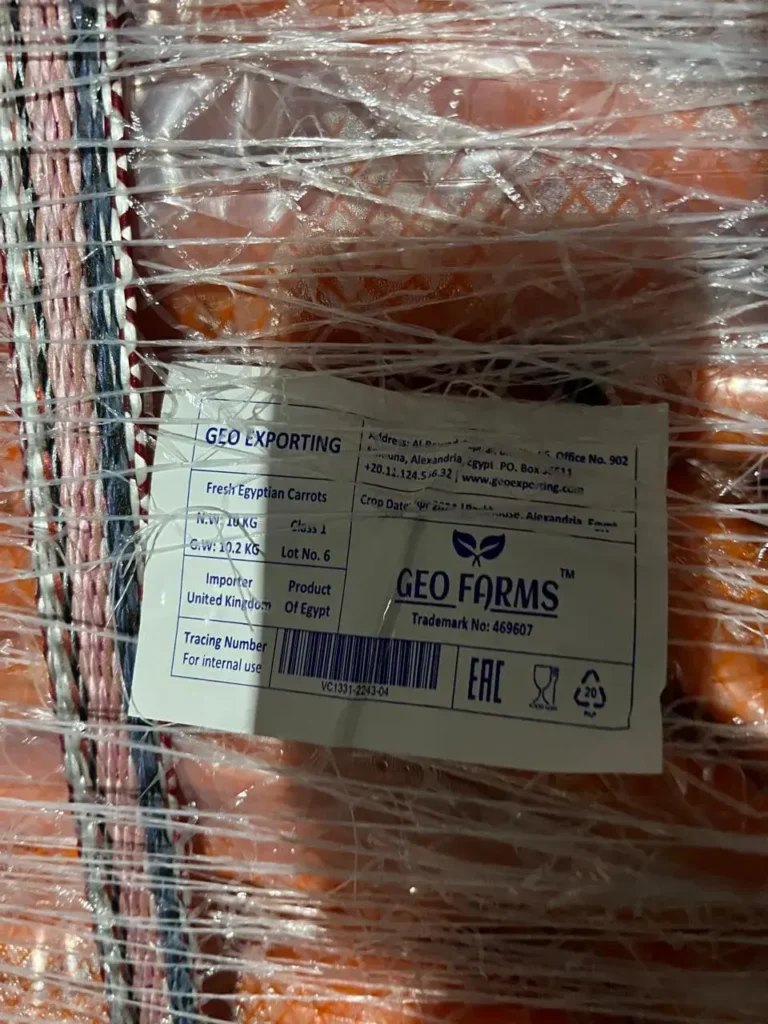 Close-up of GEO Exporting product label on a pallet of carrots. Text reads 'Importer United Kingdom', 'Class 1', 'N.W. 10 KG', and shows barcode for traceability.