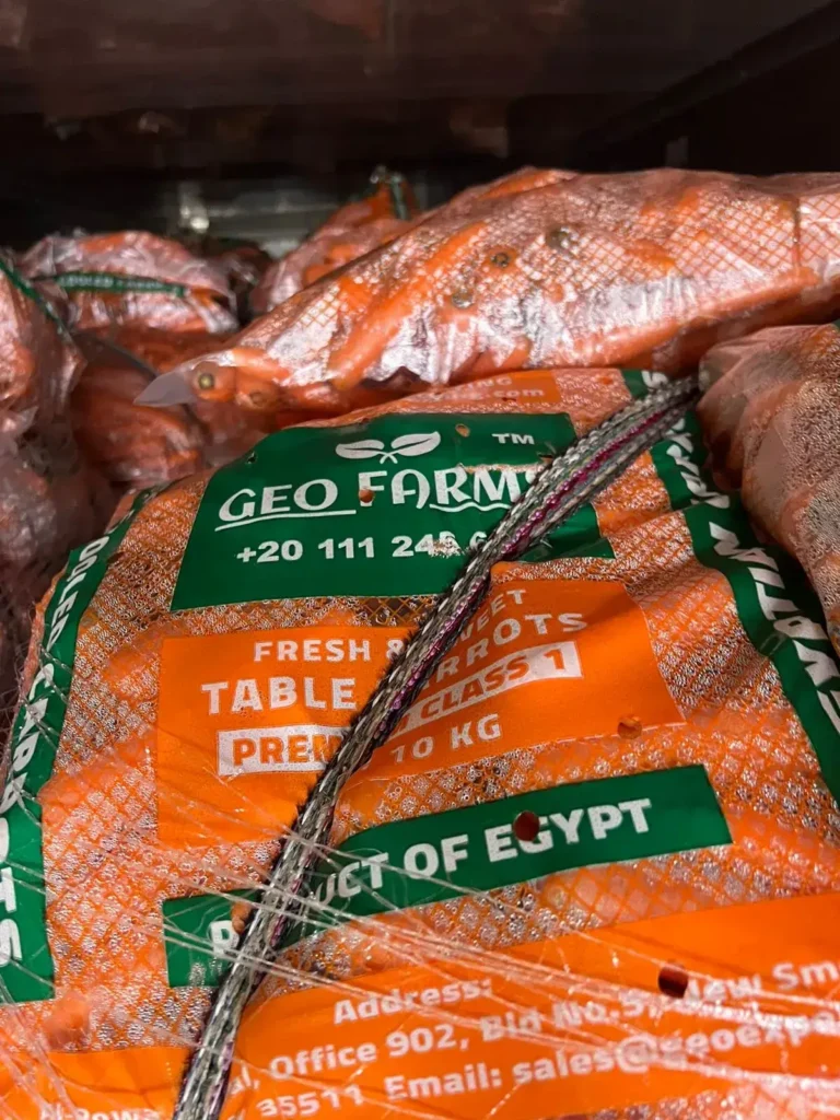 Close-up of GEO Farms 10kg mesh bag label showing 'Fresh & Sweet Table Carrots' and 'Premium Class 1'. Netting visible over the 'Product of Egypt' text.